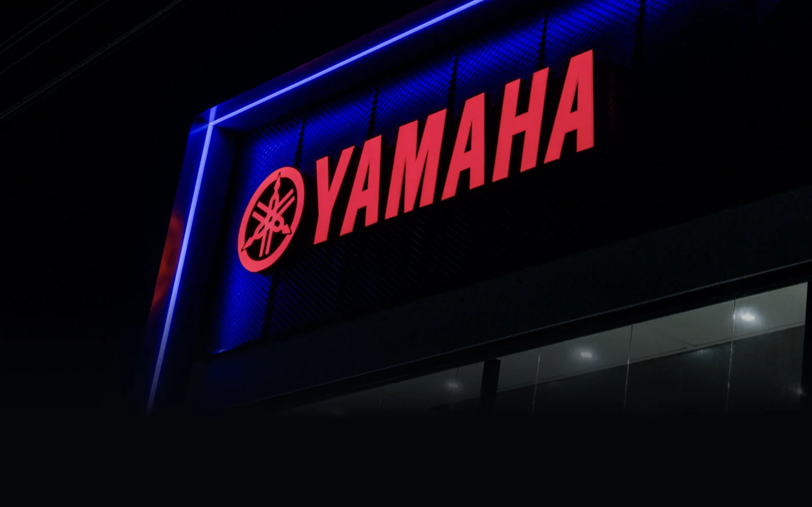 Fachada iluminada da concessionária Yamaha em Caruaru à noite, com letreiro vermelho e contorno de LED azul