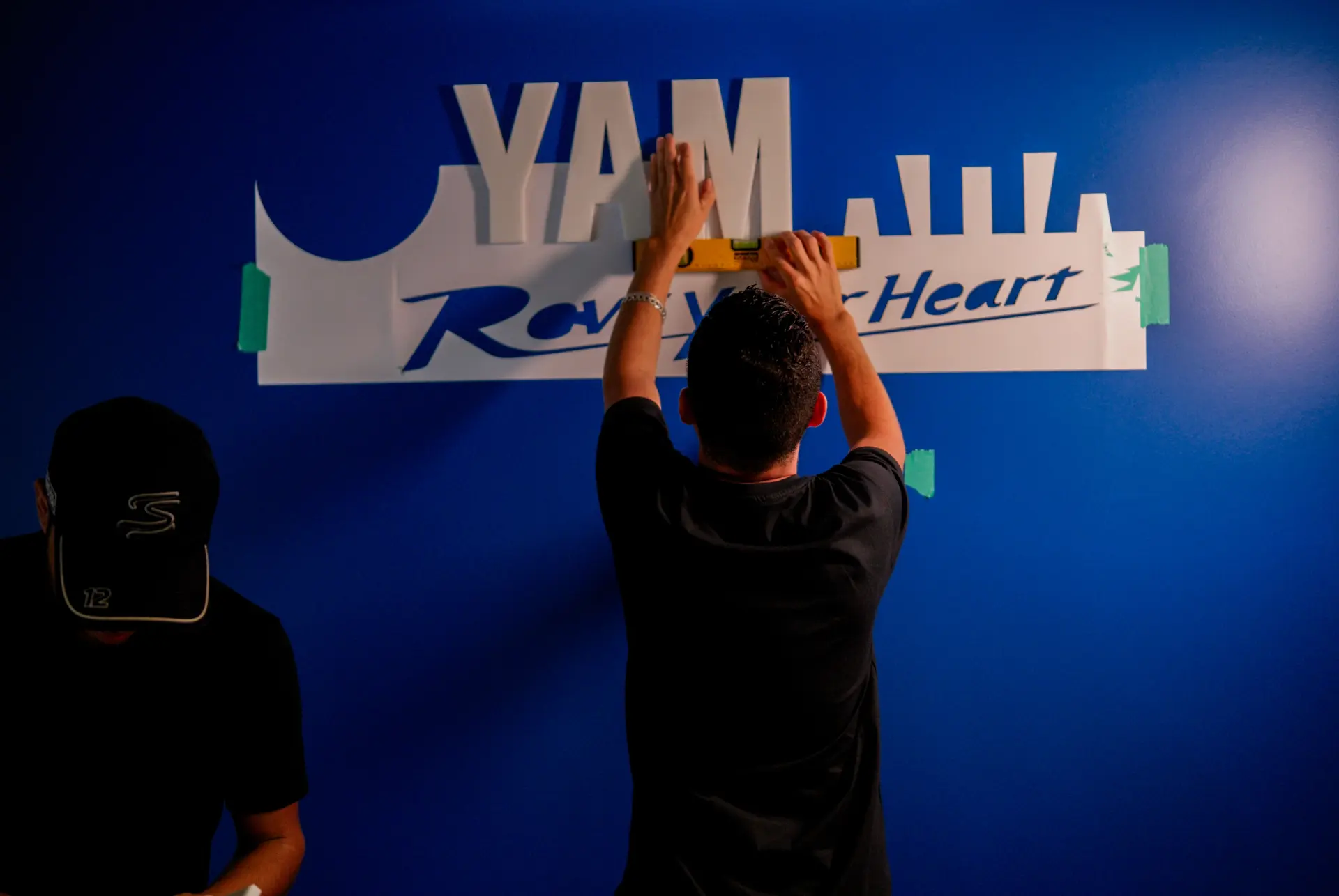 Montagem de letras do letreiro Yamaha Revs Your Heart em parede azul, com nível de precisão